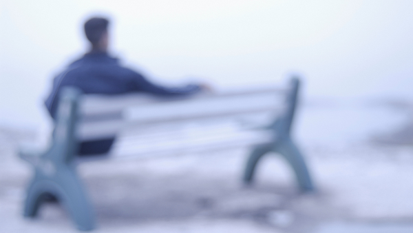 Blurred image of man sitting alone on a park bench